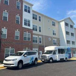 A view of a residential apartment building with parked vehicles outside on a clear day.