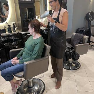 A hairstylist blow dries a client's hair in a salon.