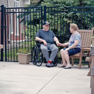 An elderly couple enjoying a moment together outdoors, with one partner in a wheelchair.
