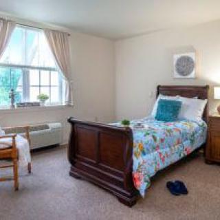 A cozy bedroom with a single bed featuring colorful bedding, accented by natural light from a large window with curtains.