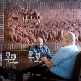 A group of men enjoying a conversation over lunch in a cozy restaurant, featuring a detailed wall sculpture in the background.
