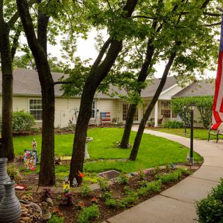 A serene backyard with a pathway, lush greenery, and an American flag.