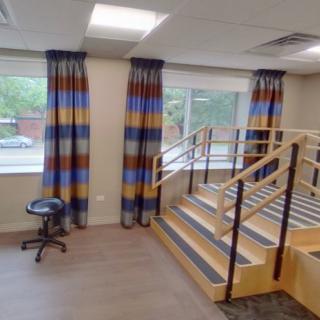 A therapy room featuring a set of stairs, colorful curtains, and large windows.
