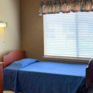 A simple bedroom with a single bed covered in blue bedding next to a window with blinds and curtains.