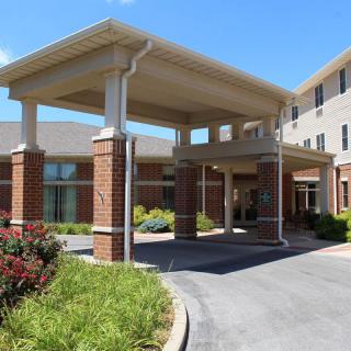 A modern building with an entrance canopy and landscaped driveway, captured during the daytime.