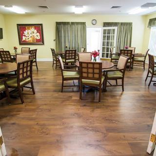 A spacious dining room with multiple tables and chairs, featuring wooden flooring and decorative artwork.