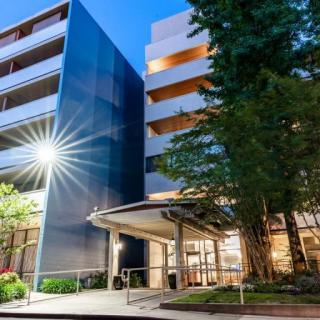 A modern multi-story building illuminated in the evening, surrounded by trees.