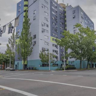 A brightly painted apartment building on a city street corner, surrounded by trees.