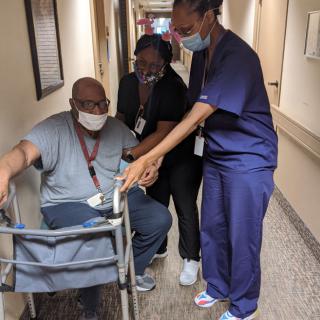 Healthcare professionals assisting a patient with a walker in a hospital corridor.