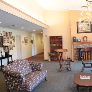 A cozy living room with a floral sofa, wooden chairs, a fireplace, and a gallery wall of photographs.