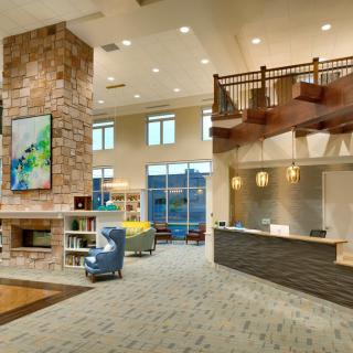 A modern lobby area featuring a stone fireplace, reception desk, and wooden staircase.