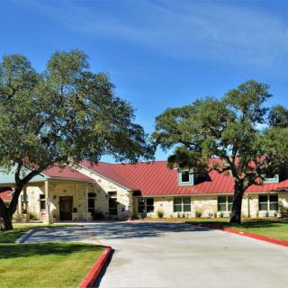 A residential building with a red roof, surrounded by trees and a driveway under a clear blue sky.