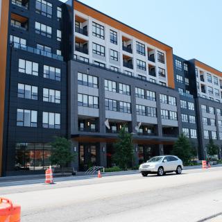 A modern multi-story apartment building alongside a city street with a parked car.
