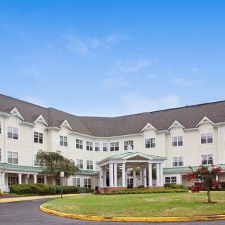 A large, white residential building with multiple windows and a landscaped front yard.