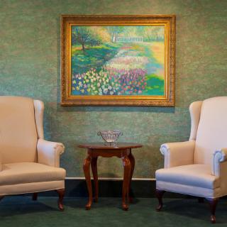A cozy living room setup with two armchairs flanking a wooden table, and a colorful landscape painting on the wall.