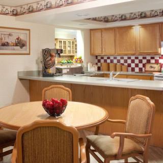 A cozy kitchen and dining area with a round table and chairs, featuring wooden cabinets and a checkered backsplash.