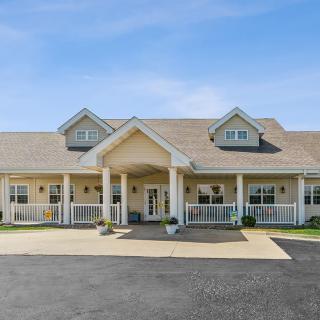 A large residential building with a gabled roof and a front porch area, captured during the daytime.