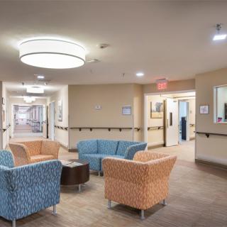 A modern waiting area with colorful chairs and overhead lighting, leading to a hallway.