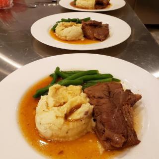 A delicious plated dinner featuring beef, mashed potatoes, green beans, and sauce.