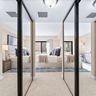 A spacious and elegantly designed bedroom with mirrored closet doors, featuring soft lighting and neutral decor.