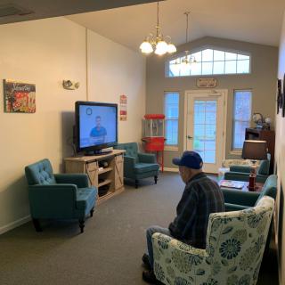 A cozy living room with a person watching television, surrounded by comfortable seating and warm lighting.