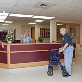 An elderly man with a walker approaches the reception desk in a healthcare facility.