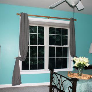 A bedroom with teal walls, featuring a window adorned with gray curtains and a metal bed frame. A vase of flowers sits on a side table.