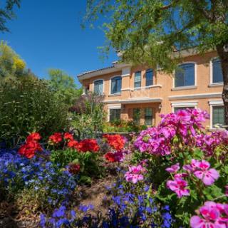 A vibrant garden filled with colorful flowers in front of a lovely house under a clear blue sky.