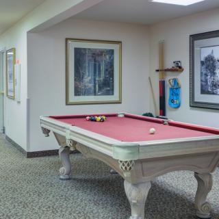 A game room with a red felt pool table, wall art, and cue sticks on a holder.