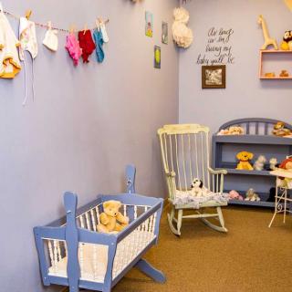 A cozy nursery room with a blue crib, rocking chair, and shelves filled with stuffed animals and toys.