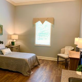 A cozy bedroom with a single bed, desk, and chair, featuring soft lighting and a large window.