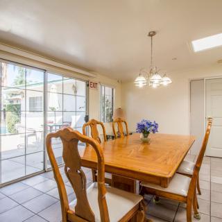 A bright dining room with a wooden table and chairs, illuminated by a chandelier and natural light from sliding glass doors.