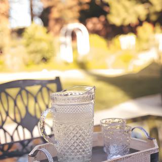 A pitcher and glasses sit on a tray outdoors in a sunny garden setting.
