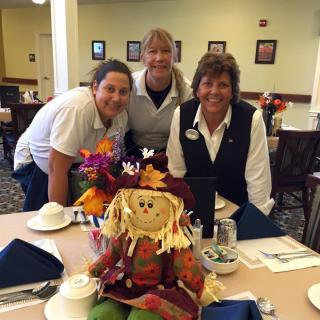 Three people posing with a scarecrow decoration on a table in a restaurant setting.