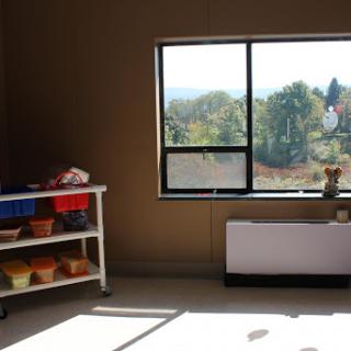 A well-lit room featuring a shelf with colorful containers and a large window offering a view of the outdoors.