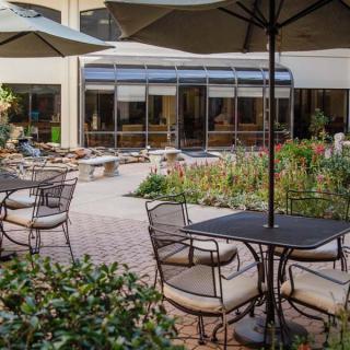 Outdoor patio with tables and chairs under umbrellas, surrounded by a garden.