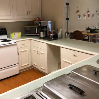 A cozy kitchen featuring a stove, microwave, and coffeemaker with ample countertop space and white cabinets.