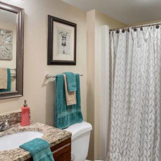 A neatly organized bathroom with a granite countertop, turquoise towels, and a patterned shower curtain.