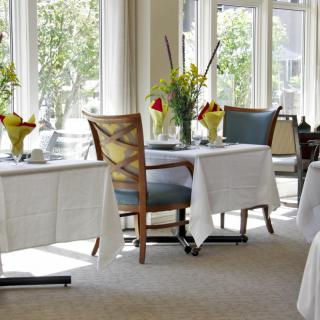 A bright and elegant dining area with tables set with white tablecloths and floral centerpieces.