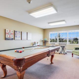 A well-lit game room featuring a pool table and comfortable seating by large windows.