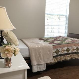 A cozy bedroom with a quilt-covered bed, a bedside lamp, and a vase of flowers.