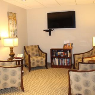 A cozy waiting room with comfortable chairs, a television, and a bookshelf.