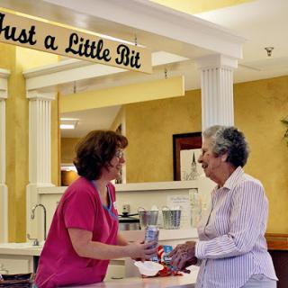 A caregiver handing a drink to an elderly resident in a warm, welcoming environment.