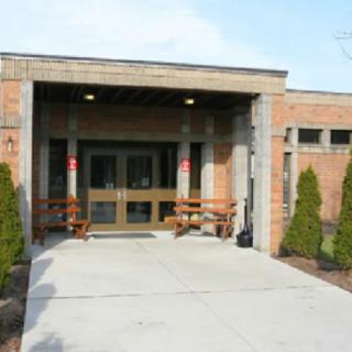 A brick building entrance with a concrete pathway and surrounding landscaping.