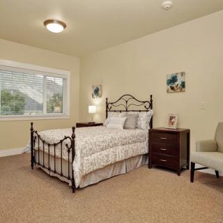 A cozy bedroom with a metal bed frame, nightstand, and an armchair by the window.
