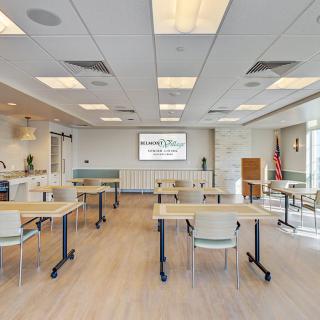 A modern conference room with tables and chairs arranged in rows facing a presentation screen.