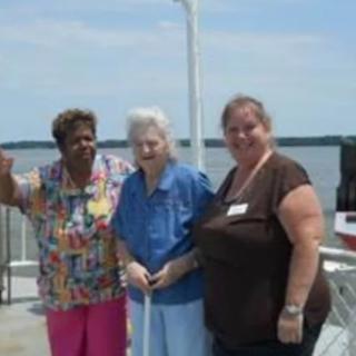 Three people smiling and posing together outdoors near a body of water.