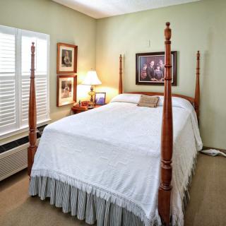 A cozy bedroom featuring a four-poster bed with white bedding, complemented by a bedside lamp and framed artwork on the walls.
