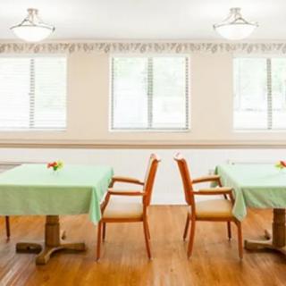 A tidy dining room with tables covered in green tablecloths and wooden chairs.