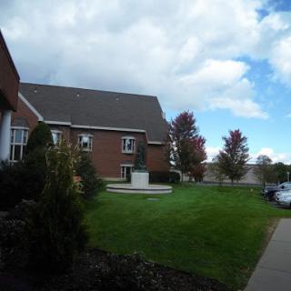 A picturesque view of a building surrounded by green grass and trees under a cloudy sky.